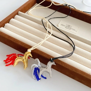 Detailed view of horse-shaped glass necklaces with gold and silver accents on velvet tray