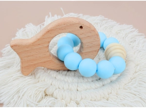 Detail of wooden fish teether and blue silicone beads on a white woven macrame mat
