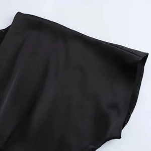 Detail eines schwarzen Satin-Midikleides mit glatter Textur und weichem Schulterfaltenwurf