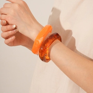 Detail showing resin wide bangles in solid orange and tortoiseshell patterns on wrist