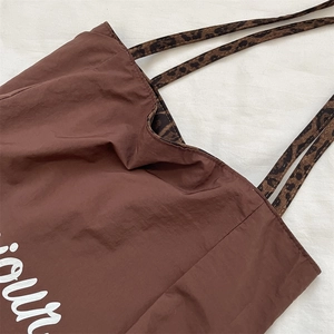 Detail of leopard print handles and dark nylon fabric on a large reversible tote bag