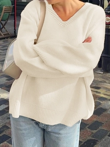 Chic off-white V-neck knitted sweater paired with casual jeans in an outdoor street setting