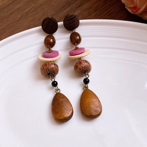 Detailed view of bohemian long wooden earrings with multi-colored beads on a white plate