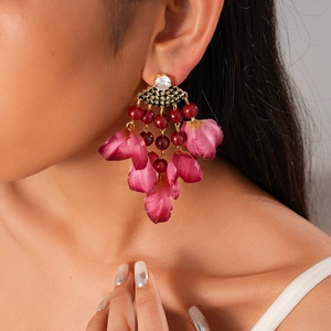 Close-up of model wearing floral earrings with dark red beads and pink fabric petals