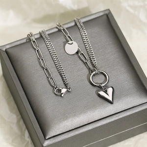 Close-up of double-layered silver heart and round tag pendants on a paperclip chain