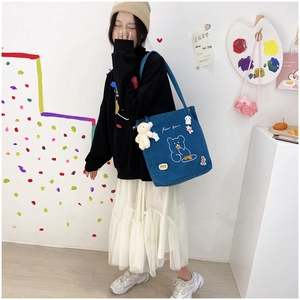 Close-up of blue corduroy tote bag featuring white cartoon bear and plush charm pendant