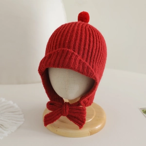 Détail du bonnet en tricot rouge pour bébé avec protège-oreilles, pompon et nœud