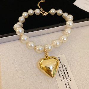 Detailed view of pearl necklace featuring a polished gold heart pendant and golden beads