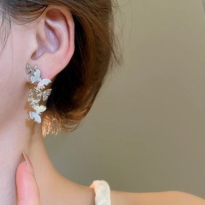 Detailed view of silver butterfly tassel earrings with white shell on a female model