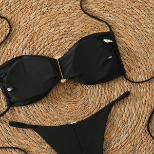 Detail of black bikini top with gold metal ring on a rustic woven straw background