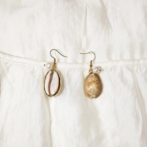 Macro shot of gold seashell earrings with natural shells and white pearls on white fabric
