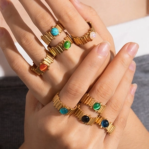 Detail of stacked gold gear rings featuring vibrant colorful cabochon gemstones on hand