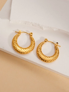 Detailed macro of golden C-shaped hoop earrings with vintage hammered metal texture on stone