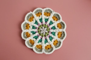 Macro detail of handmade crochet flower coasters in various colors on pink background