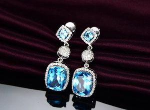 Macro shot of cushion-cut blue aquamarine earrings with halo diamonds and silver setting