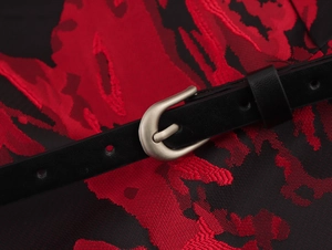 Detailed close-up of a slim black belt with a silver buckle on red floral jacquard fabric