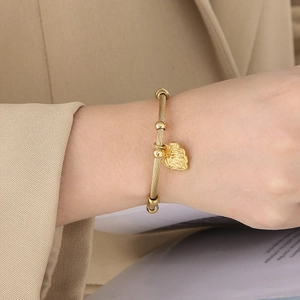 Close-up of golden twisted wire bangle with heart pendant on a beige suit sleeve