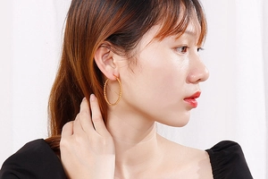 Detail view of large gold beaded hoop earrings worn by a model on a white background