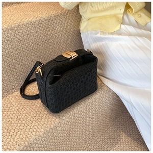 Detail of black woven texture handbag featuring elegant gold hardware and strap