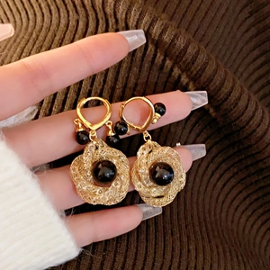 Detail of elegant gold woven mesh drop earrings with round black pearls on knit background