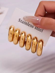 Detailed view of three pairs of chunky polished gold hollow hoops in stainless steel