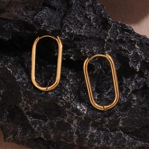 Detail of minimalist 18K gold plated oval earrings on a black textured stone surface