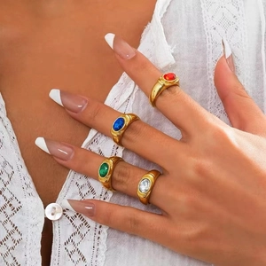 Detail of four vintage gold rings with oval colorful gemstones worn over lace fabric