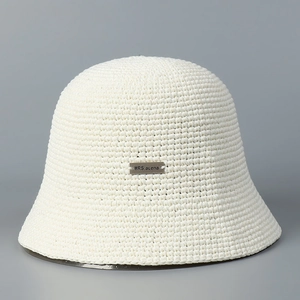 Close-up of white hand-woven bucket hat featuring a rectangular silver metal brand plaque