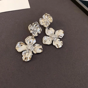 Macro detail of silver flower drop earrings with metallic petals on a dark textured surface
