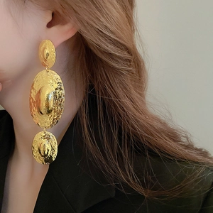 Macro shot of long gold earrings featuring three hammered metal oval geometric shapes