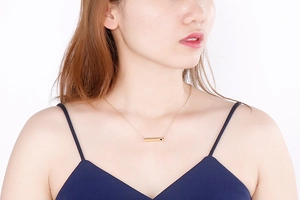 Close-up of a gold bar necklace with heart gemstone on a model with blue top