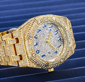 Macro side view of gold iced-out watch with blue Arabic numerals and date window