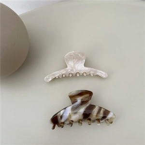 Detailed view of cream marble and amber brown acetate claw clips on neutral background