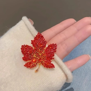 Detailed view of a red maple leaf brooch with sparkling crystals on a white knit sleeve