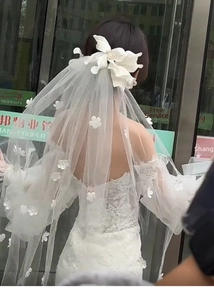 Detail of short bridal veil with 3D floral accents and off-shoulder lace wedding dress
