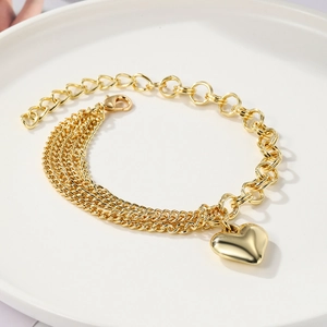 Detailed shot of gold multilayer chain bracelet with a heart pendant on white ceramic