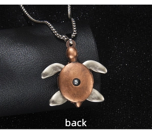 Macro shot of sea turtle pendant back in bronze and silver finish on black leather background