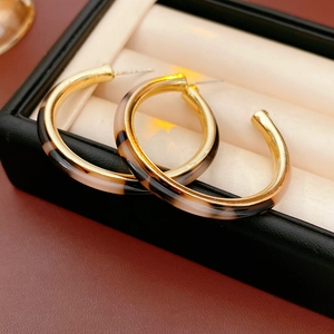 Macro shot of C-shaped amber resin and gold metal hoop earrings in a jewelry box