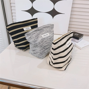 Three-piece set of striped canvas cosmetic bags with minimalist woven labels on a white surface