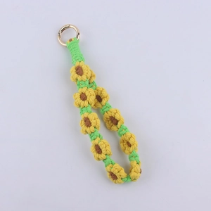Detail of handmade crochet sunflower keychain with green woven strap and golden clasp