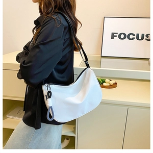 White crescent underarm bag with decorative woven knot charm shown on a model