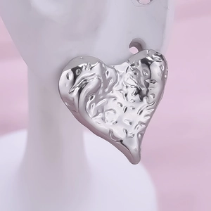 Macro shot of silver heart-shaped earrings with irregular hammered texture on model