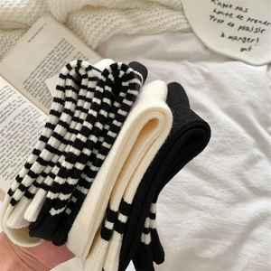 Women wool knit socks with black and white stripes shown on a soft bed setting