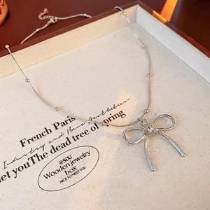 Elegant silver bow pendant necklace with beaded chain on a vintage wooden jewelry box