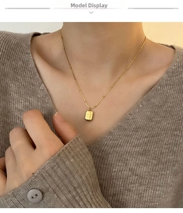 Detail of a vintage square pendant necklace in gold finish on a grey sweater