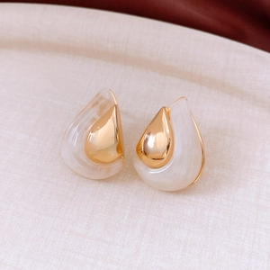 Detail of 18K gold plated teardrop earrings with cream resin inlay on beige fabric