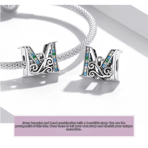Macro shot of 925 silver letter M charm with colorful zircon inlay and hollow patterns