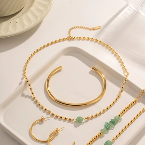 Detailed set of gold jewelry with green stone necklace, open bangle, and hoop earrings