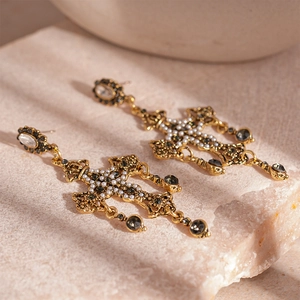Détails macro de boucles d'oreilles croix dorées avec cristaux noirs et perles blanches