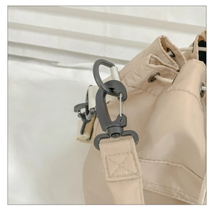 Detail of khaki nylon shoulder bag featuring black hardware hooks and drawstring closure
